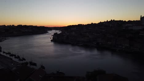 Birds-fly-in-beautiful-sunset-sky-over-Douro-River-with-docked-river-boats-in-foreground,-Porto,-Portugal