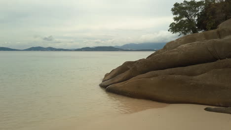 Walking-along-golden-beach-towards-eroded-rocks-in-Borneo-as-the-tide-calmly-flows-in-with-islands-in-the-background