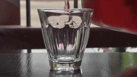 Blick-Auf-Das-Leere-Glas,-Während-Rosentee-Aus-Einer-Glasflasche-Hineingegossen-Wird,-In-Zeitlupe---720p
