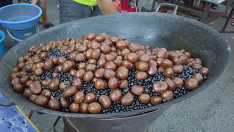 Man-shovelling-chestnut-with-hot-pebbles-using-metal-spatula-on-a-big-wok-with-smoke-coming-out-from-the-wok