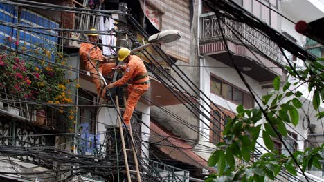 Two-utility-electrician-workers-fix-a-tangle-of-high-voltage-cables-high-on-a-utility-pole,-wide-handheld-shot