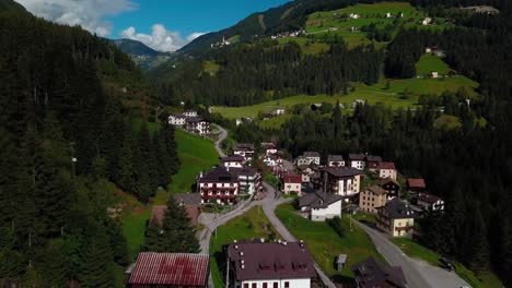 Dolomite-mountain-village-town-in-northern-Italy-with-roads-passing-through-buildings-and-homes,-Aerial-drone-flyover-reveal-shot