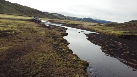 Four-Wheel-Drive-Vehicle-Crossing-River-on-Expedition-in-Iceland-Nature-Reserve-Under-Volcanic-Hills