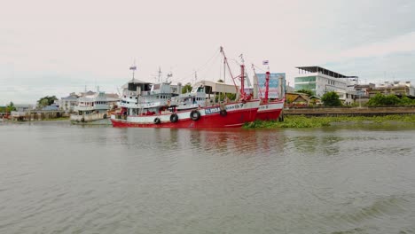 Fishing-Boats-moored-in-the-mud-at-a-river-bank-during-the-low-tide-in-Samut-Sakhon,-Thailand-and-waiting-to-be-deployed-again