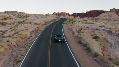 Black-convertible-Ferrari-driving-up-a-hill-through-the-Valley-of-Fire,-Nevada,-at-sunset