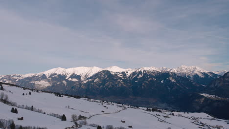 Aerial-drone-slowly-ascending,-rising-up-wide-winter-mountain-scenery-with-snowcovered-hills,-and-peaks