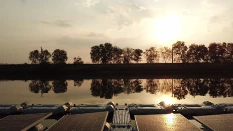 Floating-solar-farm-project-on-lake,-sun-reflecting-at-sunset,-aerial-pull-back-reveal