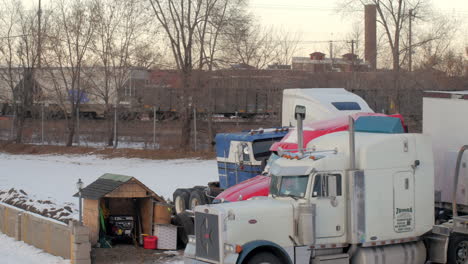 Semi-trucks-parked-for-the-winter-with-a-train-passing-in-the-background