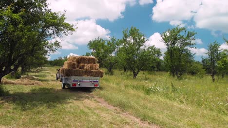 Antena-Siguiendo-Un-Coche-Que-Transportaba-Un-Remolque-Lleno-De-Pacas-De-Heno-En-Un-Campo