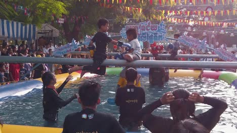 Slow-Motion-Shot-of-Two-Kids-Playing-Fighting-on-a-Pole-Above-a-Swimming-Pool