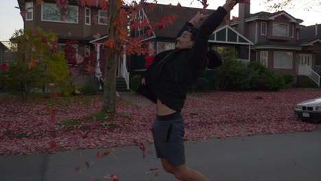 A-Young-Man-Happily-Showered-A-Bunch-Of-Maple-Leaves-In-The-Street-In-Front-Of-His-House-In-Vancouver-At-Fall-Season---Wide-Shot