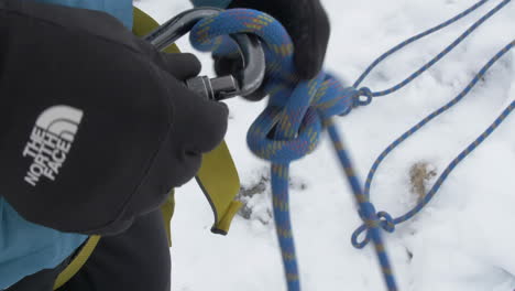 Gloved-Hands-Attach-a-Rope-to-a-Carabiner-Over-an-Icy-Surface,-Slow-Motion