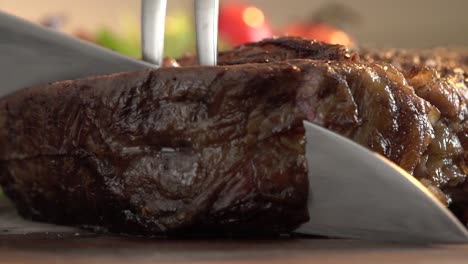 Extreme-close-up-shot-on-piece-of-steak-cutting-using-a-kitchen-knife-and-barbecue-fork