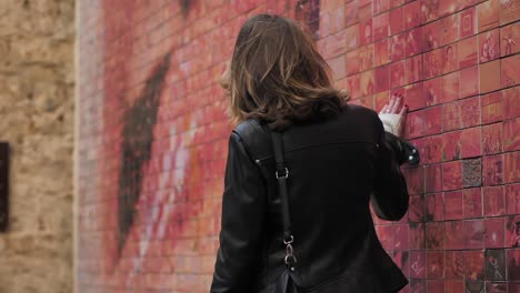 Close-view-of-back-of-woman-touching-red-photo-mosaic-wall,-slomo