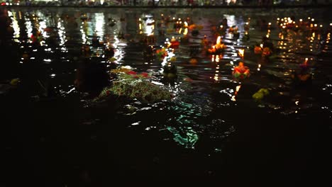Small-thai-girl-swims-among-tens-of-Loy-Krathongs-in-the-City-Canals-when-other-people-float-Krathongs-and-pray-at-night-during-Loi-Krathong-festival-in-Korat,-Thailand