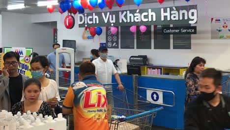 Un-Trabajador-De-Un-Supermercado-Almacena-Desinfectante-De-Manos-En-Primer-Plano-Mientras-Los-Compradores-Vietnamitas-Con-Máscaras-Faciales-Pasan-Al-Fondo-En-La-Ciudad-De-Ho-Chi-Minh,-Vietnam,-El-7-De-Marzo-De-2020