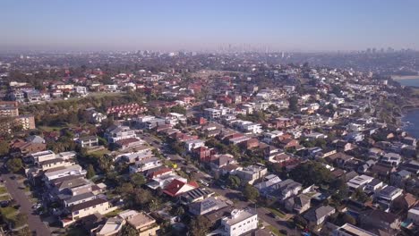 Luftaufnahme-Von-Wohnhäusern-In-Der-Nachbarschaft-Mit-Blick-Auf-Die-Stadt-Sydney-CBD-Und-Dem-Berühmten-Strand-Im-Hintergrund