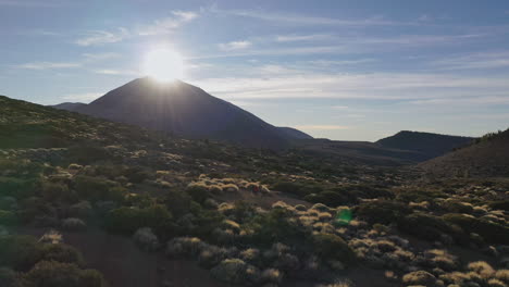 Three-hikers-standing-on-the-hillside-below-the-Pico-de-Teide-mountain-on-Canary-Islands-and-watching-the-Sun-setting-behind-its-summit-amongst-rocks-and-bushes