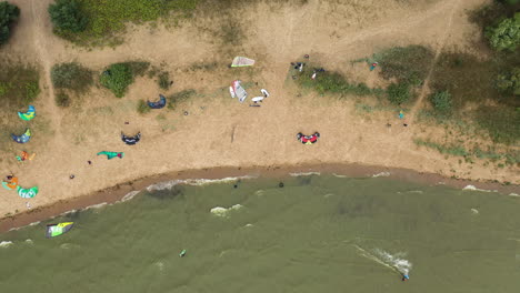 AERIAL:-Top-View-of-the-Beach-Filled-With-Kite-Surfers-Preparing-to-Kite-on-a-Green-Colour-Sea