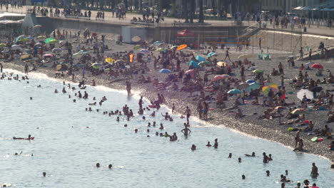 Crowded-Pebble-Beach-in-Nice-during-Summer,-People-Swimming-in-the-Sea