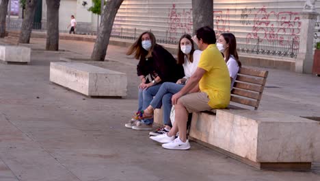 Family-wearing-face-protection-mask-sitting-on-bench-in-Merced-square