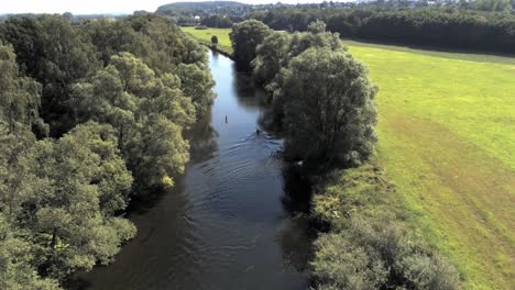 Lone-kayaker-paddles-on-Ruhr-river-among-farmland-on-hot-summer-day,-drone-aerial