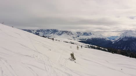 Zwei-Personen-Wandern-An-Einem-Bewölkten-Tag-Mit-Schneeschuhen-Den-Verschneiten-Berg-Hinauf,-Im-Hintergrund-Pale-Di-San-Martino