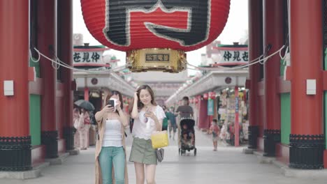 Dos-Jóvenes-Japonesas-Tomándose-Selfies-En-La-Puerta-Kaminarimon-Senso-ji-En-Asakusa,-Tokio,-Japón