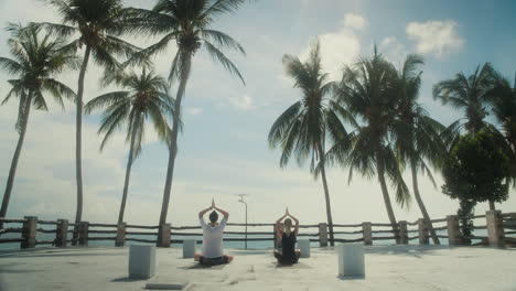 Panorama-of-rooftop-with-people-doing-morning-yoga-against-palm-trees-and-sea-view