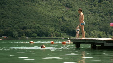 Male-Child-Outdoors-In-Summer-is-afraid-to-Jump-Off-Wooden-Jetty-Into-Lake-Water
