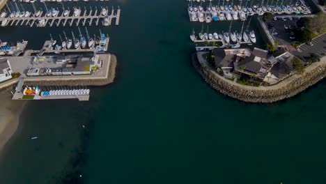 Aerial-tilt-up-reveals-entrance-to-crowded-boat-harbor-docks-and-blue-sky