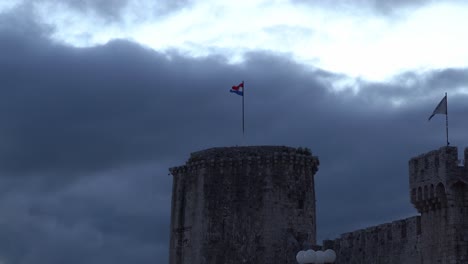 Torre-Kamerlengo,-En-La-Ciudad-De-Trogir-En-Croacia,-Al-Atardecer-Con-Una-Larga-Bandera-Croata-Y-Nubes-A-La-Deriva