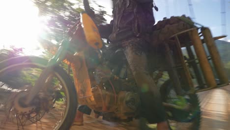 Trabajador-De-La-Aldea-Que-Conduce-Una-Motocicleta-Con-Cestas-De-Madera-A-Través-Del-Puente-Hacia-El-Camino-De-Tierra,-Vietnam