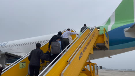 Airplane-passengers-boarding-jet-walking-up-stairs-to-entrance,-Noi-Bai-Intranational-Airport,-Hanoi,-Vietnam