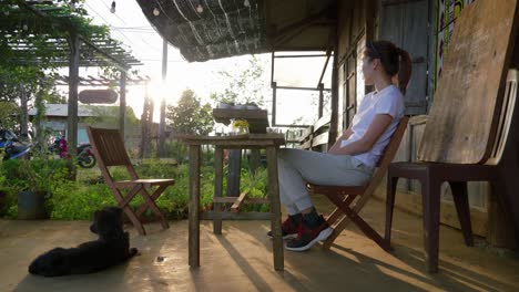 Asiatische-Frau-Sitzt-Draußen-Mit-Einem-Hund-Und-Trinkt-Aus-Einem-Glas,-Tagsüber,-Vietnam