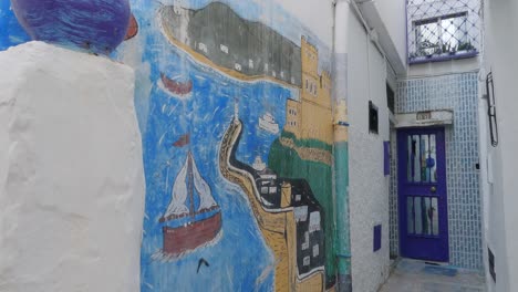 Gemälde-Auf-Weißer-Wand-In-Einer-Kleinen-Gasse-In-Der-Medina-Von-Tanger,-Nach-Unten-Geneigte-Aufnahme