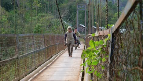 Villagers-walking-and-driving-motorbike-across-wood-and-rope-bridge-over-river,-Vietnam