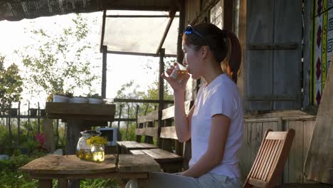 Young-Asian-woman-sipping-a-drink-from-a-glass-while-sitting-on-porch-outdoors,-Vietnam