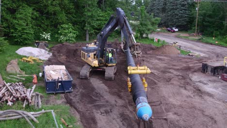 Machinery-installing-water-main-pipe-in-Michigan,-aerial-pull-out