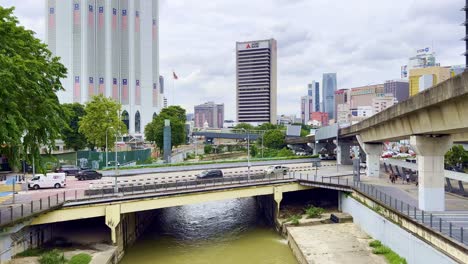 High-angle-shot-of-traffic-movement-over-a-bridge-with-a-narrow-river-passing-by-below-in-Kuala-Lumpur-city,-Malaysia-at-daytime