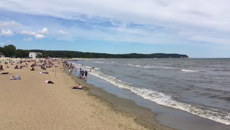Sopot-beach-with-water-waves-and-a-lot-of-people-relaxing,-Poland-during-summer