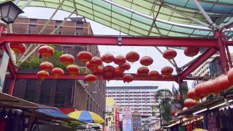Low-angle-shot-taken-while-walking-under-red-colored-lanterns-hanging-over-a-roadside-marketplace-in-Kuala-Lumpur,-Malaysia-at-daytime