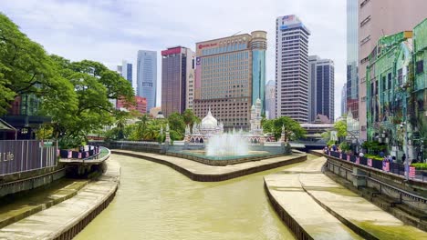 Shot-of-river-flowing-in-front-of-Sultan-Abdul-Samad-Jamek-mosque,-surrounded-by-tall-buildings-in-Kuala-Lumpur,Malaysia-at-daytime