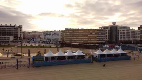 Caparica-Surf-Fest-tents-venue-During-a-cloudy-morning,-Aerial-Orbiting-shot-over-Beach