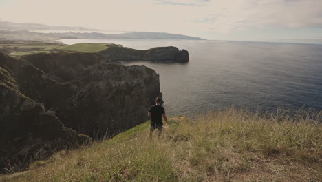 Wide-view-of-man-walking-to-edge-of-cliff-at-Azores-coastal-landscape