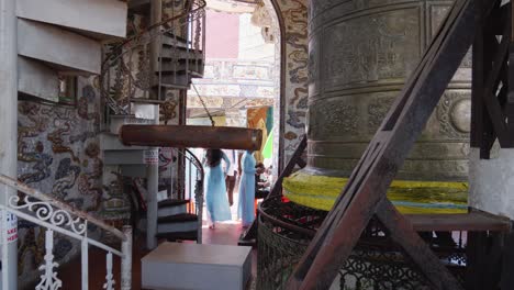 Woman-in-blue-dress-walks-from-a-Buddhist-Bell-With-Suspended-Log-Inside-The-Linh-Phuoc-Temple-In-Vietnam