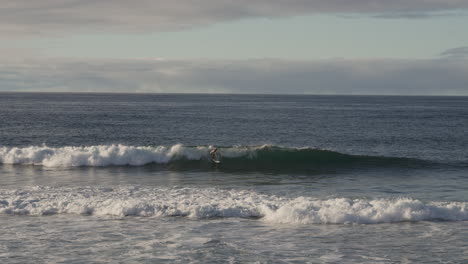 Wide-pan-of-man-surfing-on-waves-by-Azores-coast-and-ocean-horizon