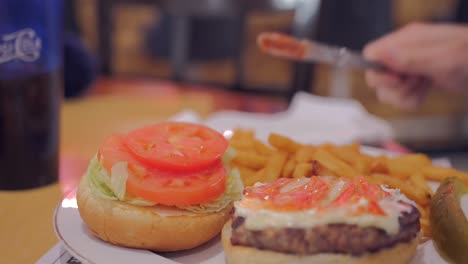 Customer-Spreading-Dressing-On-Burger-Patty-In-A-Plate-Of-Burger-Meal-At-American-Diner