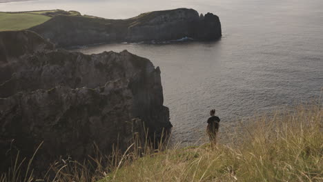 Handheld-shot-of-man-standing-on-grassy-cliff-by-ocean-at-the-Azores