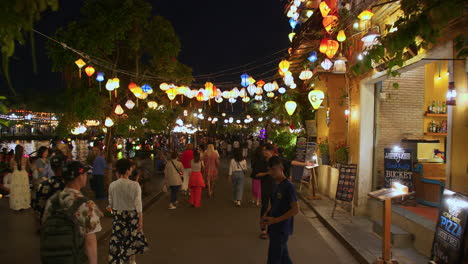 POV-shot-of-local-people-and-tourists-walking-tour-in-the-ancient-town-of-Hoi-An-decorated-with-colorful-lanterns-alongside-river-at-night,-Vietnam